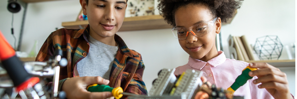 Two children wearing safety glasses working together on an electronics project